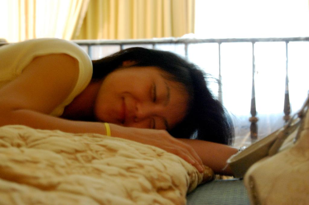 Eine Frau liegt auf einem Bett und lächelt, mit einem Vorhang im Hintergrund.