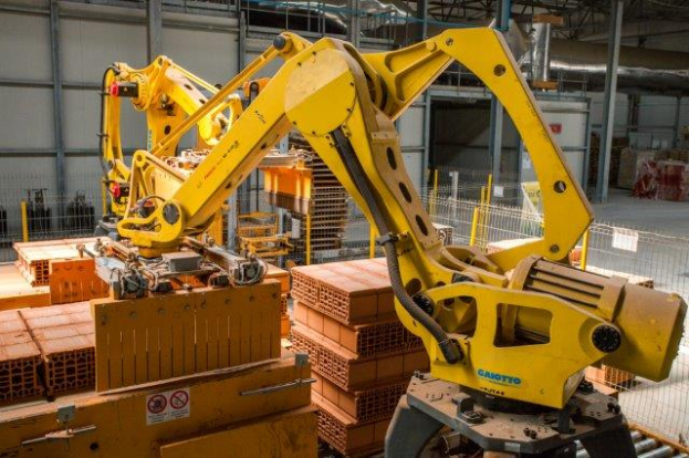 Ein großes Lager voller numerous boxes, Kräne und verschiedene industrielle Ausrüstung, mit einem Zaun und Pfählen im Vordergrund und einer Wand im Hintergrund.