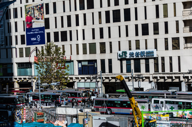 Eine belebte Stadtstraße mit zahlreichen Fahrzeugen, Fußgängern, Gebäuden und verschiedenen städtischen Elementen, einschließlich eines prominenten Fahrzeugs im Vordergrund.