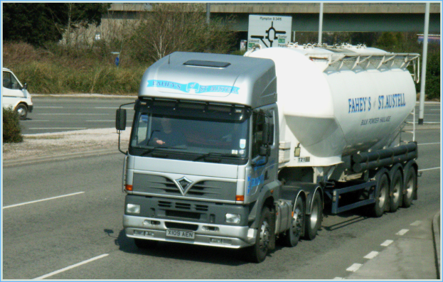 Ein Lkw mit Fahrer auf einer Straße, mit einem Van auf der Gegenfahrbahn, Bäumen und einer Brücke im Hintergrund.