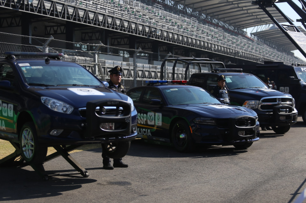 Eine Gruppe von Polizeiwagen vor einer Rennstrecke geparkt, mit uniformierten Personen auf der Straße stehend, mit einem Stadion und Maschendrahtzaun im Hintergrund.