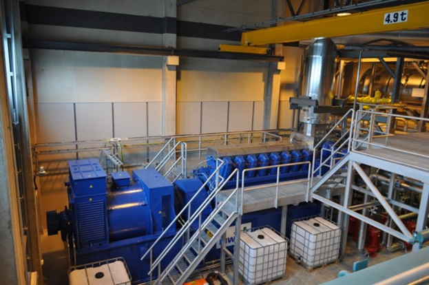 Ein Fabrikinnenraum mit Tr├Ągern, einer Treppe, einem Gel├Ąnder, Containern, Lichtern, Rohren und W├Ąnden.