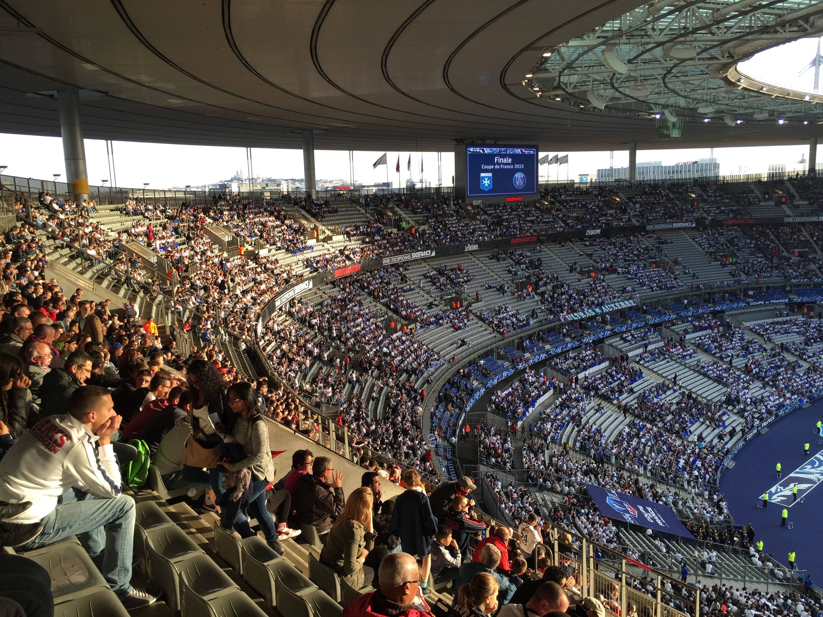 Große Zuschauermenge im Allianz Arena Stadion in München, Deutschland, bei einem Fußballspiel mit einer Bühne, Fahnen, Stangen und einem Bildschirm im Hintergrund.