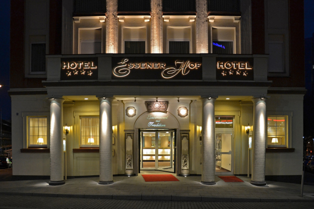 Das Essenerhof Hotel in Berlin, Deutschland, ein mehrstöckiges Gebäude mit Fenstern, Türen, Säulen und Lichtern, mit einem Namensschild, einer Straße davor und Fahrzeugen auf der rechten Seite, unter einem sichtbaren Himmel.