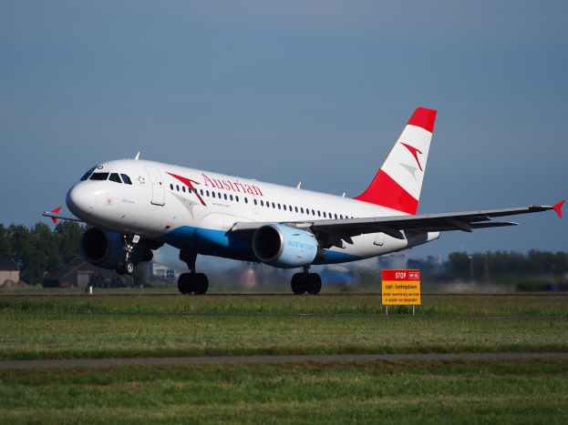 Ein Airbus A320-200 der Austrian Airlines startet vom Frankfurter Flughafen, mit einem Schild im Vordergrund, Gras, Bäumen und Gebäuden im Hintergrund und einem klaren blauen Himmel.