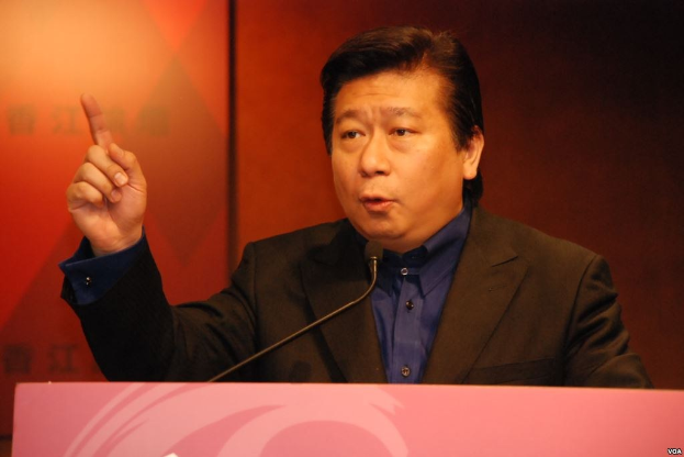 Ein Mann in Anzug und Krawatte, der eine Rede an einem Rednerpult mit Mikrofon hält und wie ein politischer Wissenschaftler mit ernster Miene wirkt.