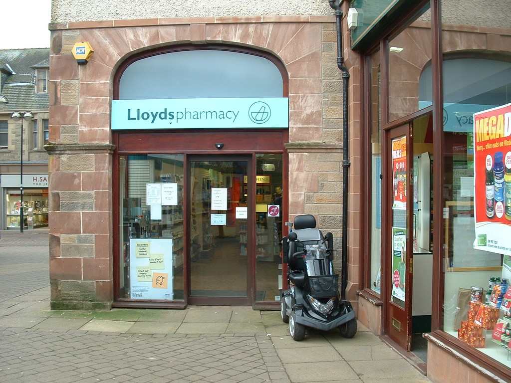 Eine Apotheken-Filiale mit einem vor dem Gebäude geparkten Fahrzeug und einem Gebäude in der linken Ecke.