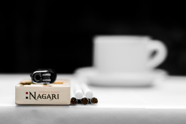 Ein Tisch mit einer Tasse und einem Unterteller, Zigaretten, Müll und einer Schachtel.