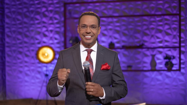 Stephen Colbert, Moderator von 'The Daily Show with Trevor Noah', steht auf einer Bühne und hält ein Mikrofon, trägt einen Anzug und eine Brille, hinter ihm ist ein Scheinwerfer und ein Ständer zu sehen.