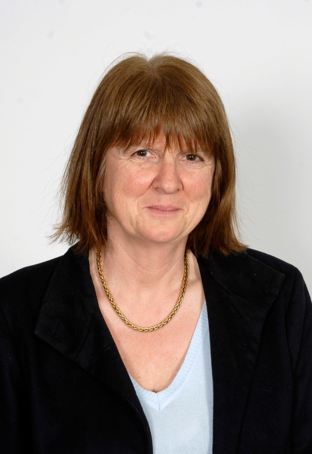 Eine Frau mit braunen Haaren, die einen schwarzen Mantel und ein weißes T-Shirt trägt.