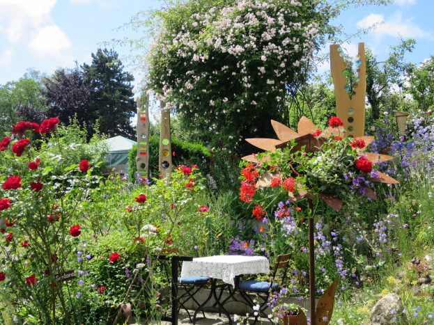 Ein Garten voller bunter Blumen und Pflanzen, mit einem Tisch mit einer Decke und Stühlen, umgeben von Bäumen unter einem bewölkten Himmel auf der Chelsea Flower Show.