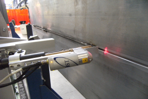 Eine Laserschneidmaschine in einer Fabrik, die helles Licht emittiert, mit einer Wand auf der rechten Seite und Gegenständen im Hintergrund.