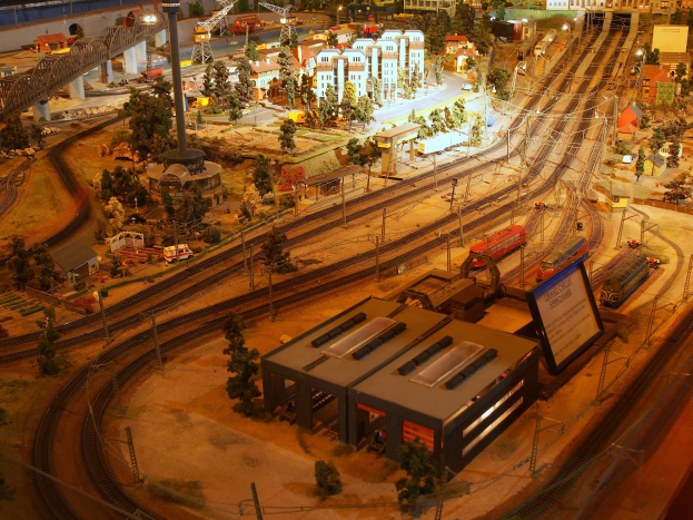 Eine detaillierte Modelleisenbahnausstellung in einem Museum, die Gebäude, Bäume, Schienen, Fahrzeuge, Pfosten, Lichter und andere Gegenstände enthält, die eine belebte Stadtlandschaft darstellen.