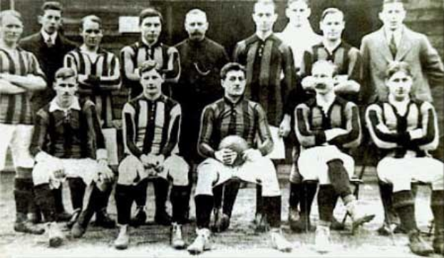 Ein Schwarz-Weiß-Foto einer Fußballmannschaft, einige stehen, einige sitzen, vor einer Wand, mit dem Text "Ballymena Football Club" unten.