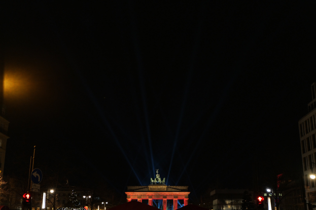Brandenburger Tor in Berlin nachts, von Straßenlaternen beleuchtet, umgeben von Gebäuden, Bäumen, Pfählen, Verkehrszeichen, Schildern und Zelten unter einem dunklen Himmel.