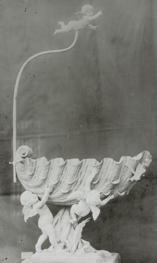 Ein Schwarz-Weiß-Foto einer Skulptur mit zwei Cherubim auf einem Sockel, deren Arme ausgebreitet sind, als würden sie sich umarmen, vor einer Wand im Hintergrund.