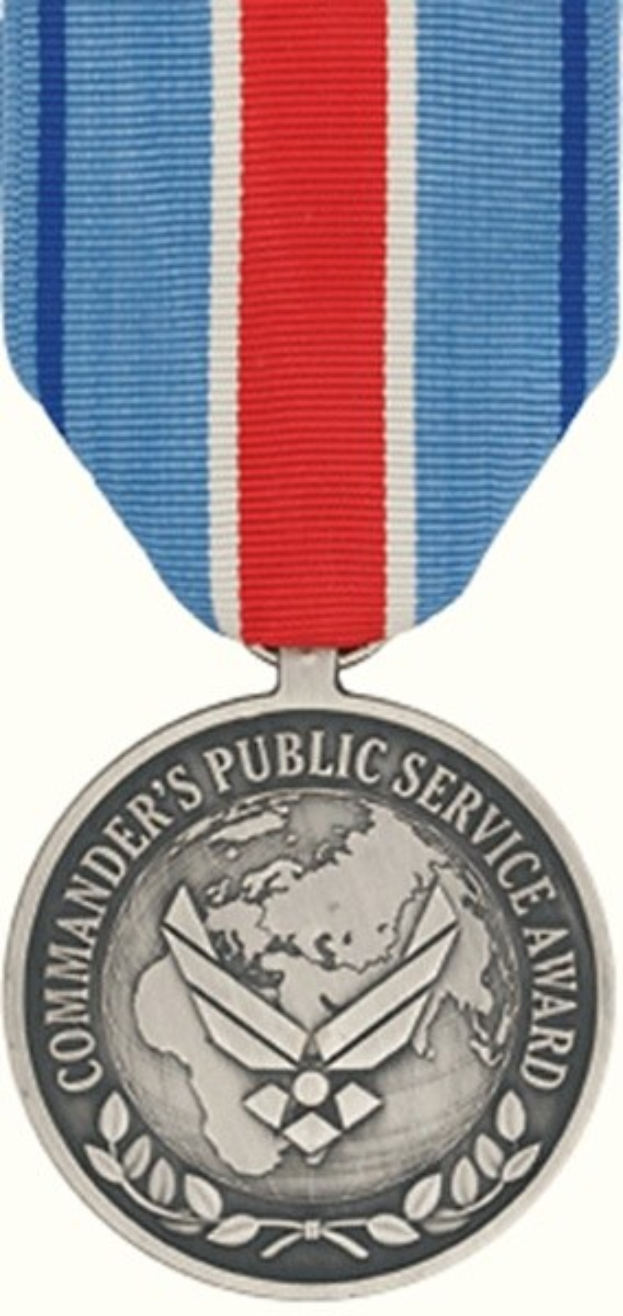 Eine silberne Medaille mit einem rot-weiß-blauen Band, beschriftet mit 'Commander's Public Service Award', vor einem weißen Hintergrund.