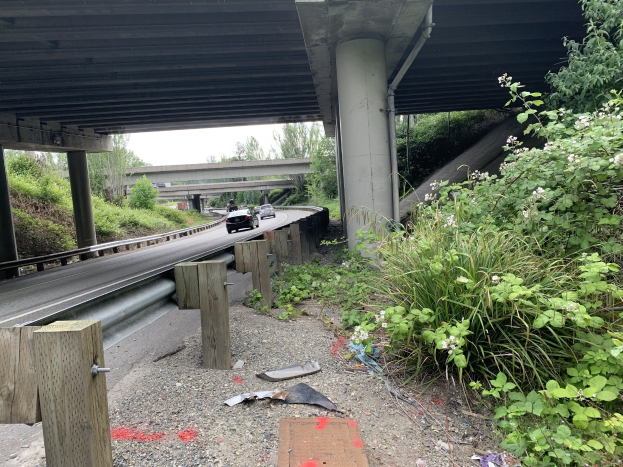 Auto fährt unter einer Brücke mit Trömmern auf der Stra√enseite, umgeben von Vegetation und einem klaren Himmel, wahrscheinlich die Nachwirkung eines tödlichen Unfalls auf dem I-95.
