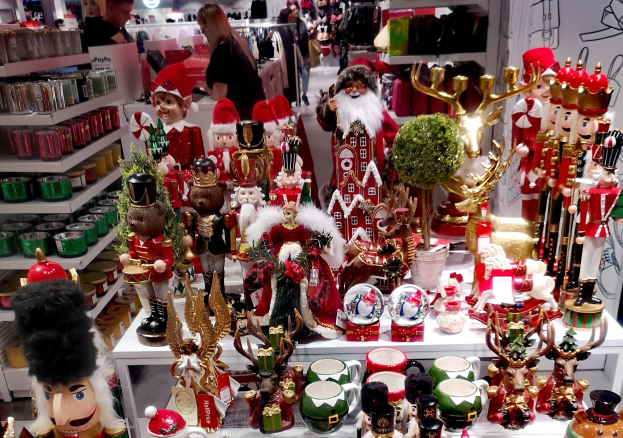 Ein Geschäft mit weihnachtlich dekorierten Tischen, Regalen mit Waren und festlicher Beleuchtung mit Menschen im Hintergrund.