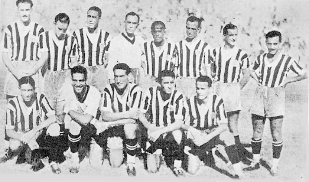 Ein Schwarz-Weiß-Foto einer Fußballmannschaft, bei der einige Spieler stehen und andere auf dem Boden sitzen, mit Text unten.