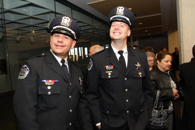 Zwei strahlende Beamte im Vordergrund, Menschen in der Mitte, Glasfenster links, Lampen und Decke oben und Säulen und Menschen rechts.