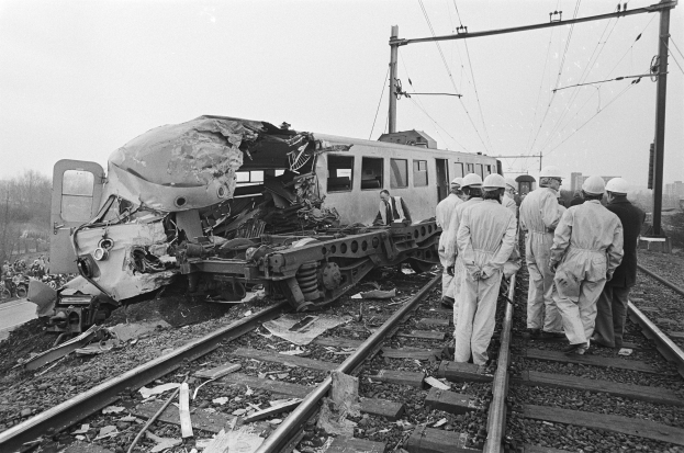 Ein Schwarz-Weiß-Bild einer Zugkollision auf den Schienen mit Einsatzkräften in Helmen und sichtbaren Infrastruktur drumherum.