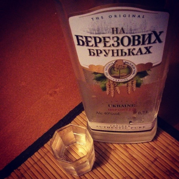 Ein klares Glas mit einer goldenen Flüssigkeit, wahrscheinlich Alkohol, das auf einer dunklen Matte steht.