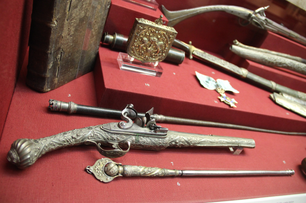 Vitrine mit verschiedenen Waffen, einschließlich einem Steinschlossgewehr, ordentlich auf einem roten Tisch angeordnet.