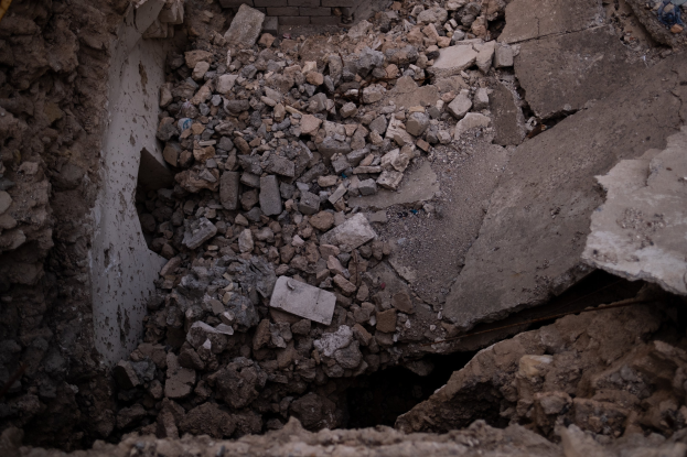 Zusammengebrochenes Gebäude mit einem großen Loch im Boden, umgeben von Trömmern und einer sichtbaren Leitung, die Erdbeeben-Schäden anzeigt.