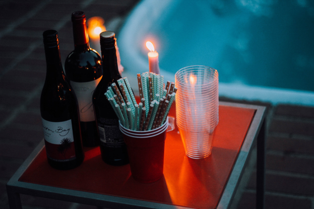 Ein Tisch am Swimmingpool mit zwei Weinflaschen, einer Kerze, Gläsern und Strohhalmen, was auf eine entspannte Nacht im Freien hindeutet.