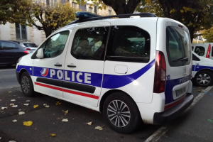 Ein Polizeiwagen parkt am Straßenrand, umgeben von Gebäuden mit Fenstern, Bäumen und zerrissenen Blättern auf dem Boden.