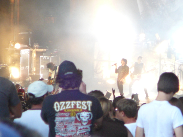 Eine Gruppe von Menschen in verschiedenen Kleidern, einige mit Kappen, in der Nähe von Musikinstrumenten wie einer Gitarre und einem Mikrofon, mit Bühnenbeleuchtung.