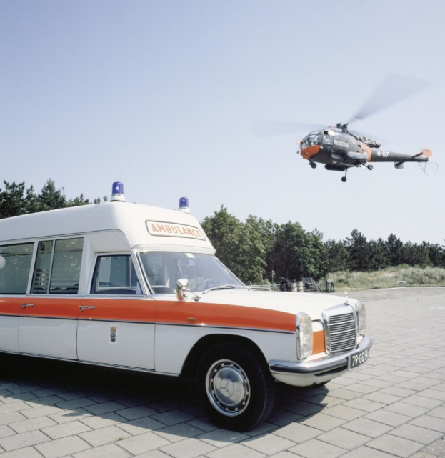 Ambulanz vor einem Hubschrauber mit Bäumen und einem klaren blauen Himmel im Hintergrund geparkt.