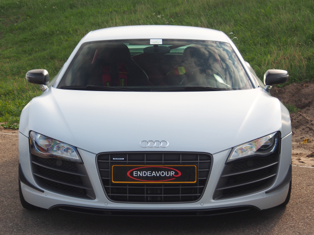 Ein weißes Audi R8 steht am Straßenrand, umgeben von grünem Gras.