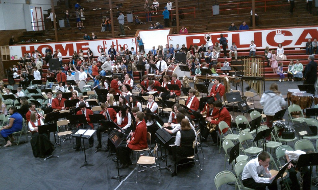 Eine Gruppe von Kindern sitzt auf Stühlen in einem Stadion bei einem Musikunterricht, mit Stadionplätzen im Hintergrund.