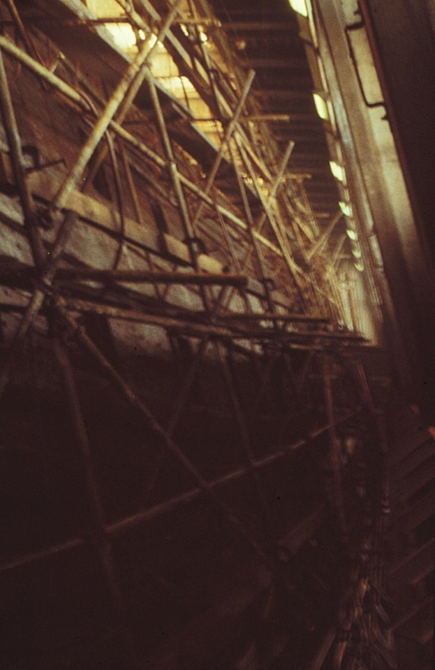 Ein Gebäude in Bau mit ausgedehntem Gerüst an seiner Seite, beleuchtet von Lichtern oben.