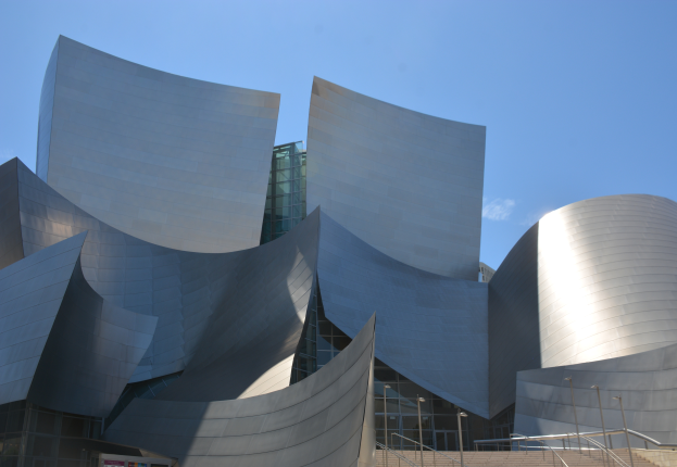 Das ARTIST Concert Hall in Los Angeles, ein modernes Gebäude mit Glaswänden und Treppen mit Geländern, die zur Eingangstür führen, umgeben von Laternenmasten, mit einer Tafel mit Text im Vordergrund und einem bewölkten Himmel im Hintergrund.