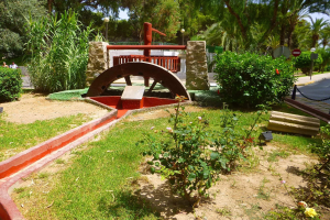 Minigolfanlage in einem Park mit Grünfläche, Straße, Fußgängern, Hinweisschildern und einem blauen Himmel.