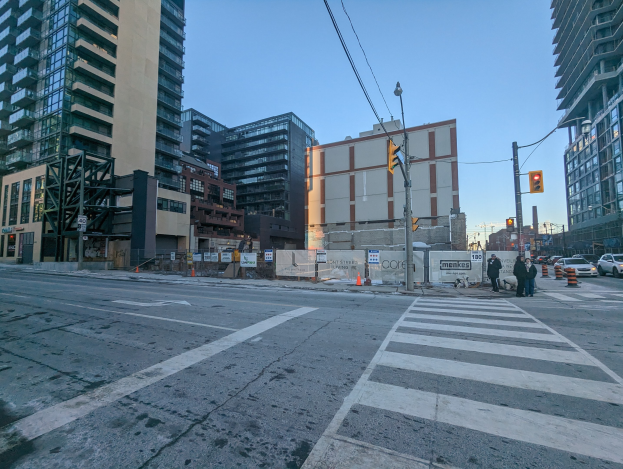 Eine Stadtstraße mit hohen Gebäuden, Fahrzeugen, Fußgängern, Verkehrs-Infrastruktur und einem klaren Himmel.