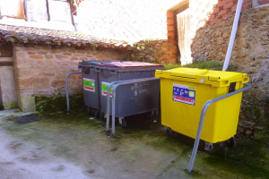 Zwei gelbe und graue Mülltonnen mit Rollen nebeneinander vor einem Gebäude mit einer Wand und einem Fenster.
