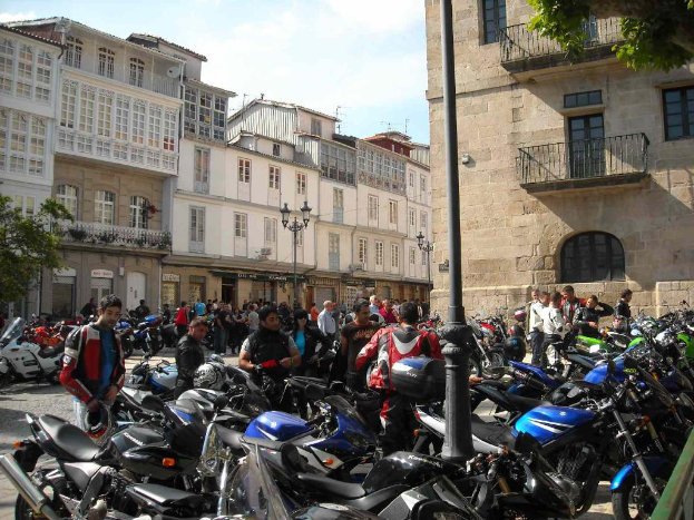 Ein cremefarbenes Gebäude mit zahlreichen Fenstern, angrenzend an ein Backsteingebäude mit einem Metallbalkon, mit mehreren geparkten Fahrrädern und Menschen, die vor dem Gebäude sprechen.