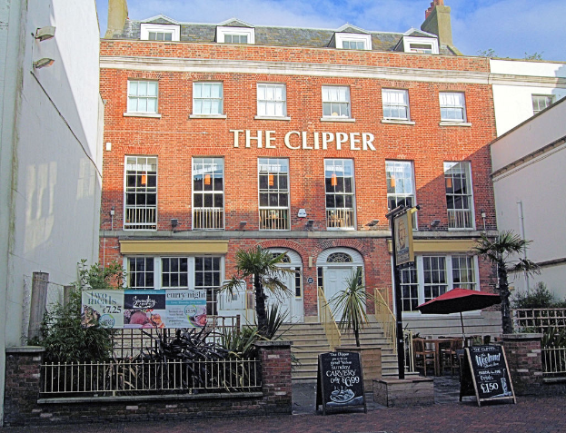 Ein Restaurant mit vielen Fenstern und zwei Türen, umgeben von Bäumen, Brettern und einem weißen Zaun.