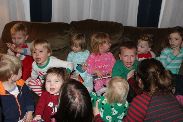 Eine Gruppe von Kindern sitzt auf einem Sofa in einem Raum, jeder hält ein Mobiltelefon in der Hand, mit einer Frau rechts und einem Vorhang oben im Bild.