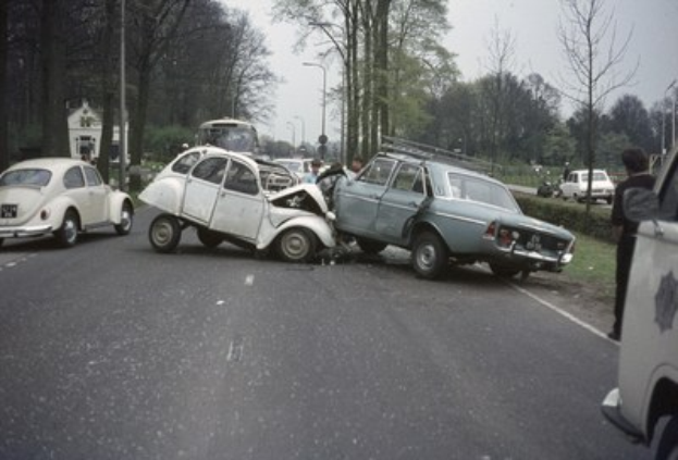 Zwei beschädigte Autos am Straßenrand mit Menschen in der Nähe, umgeben von Bäumen, Polen, Gebäuden und einem klaren blauen Himmel.