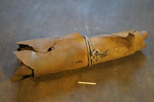 Ein brauner Papiertütenbeutel in Form einer Granate mit Henkel, zugebunden mit einem Seil und einer Zigarette daneben auf einem Tisch.