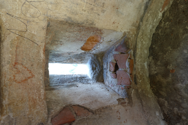 Kleines Fenster mit Graffiti in einem Steinbogen innerhalb einer Backsteinmauer.