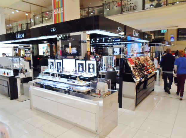 Ein Geschäft voller verschiedener Kosmetikarten, mit Menschen, die herumlaufen, Regalen, die mit Produkten gefüllt sind, und Schildern, die verschiedene Abschnitte anzeigen.