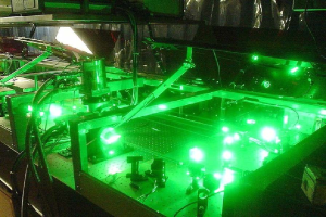 Eine Laser-Maschine auf einem Tisch, die grünes Licht abstrahlt, mit sichtbaren Komponenten und angeschlossenen Kabeln.
