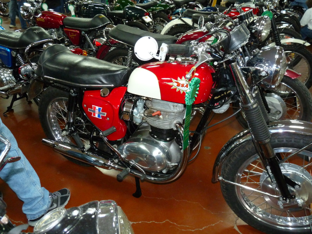 Eine Gruppe von Nitro-Bikes mit einem Mann in einem weißen Hemd und Hose, der in der oberen rechten Ecke steht, zwei Beine in Jeans und Schuhen in der unteren linken und oberen linken Ecke sichtbar.