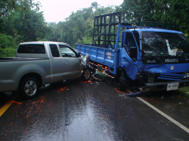 Ein schwerbeschädigter Lkw mit eingedrückter Front und verbeulter Karosserie liegt am Straßenrand neben Bäumen unter einem klaren blauen Himmel.